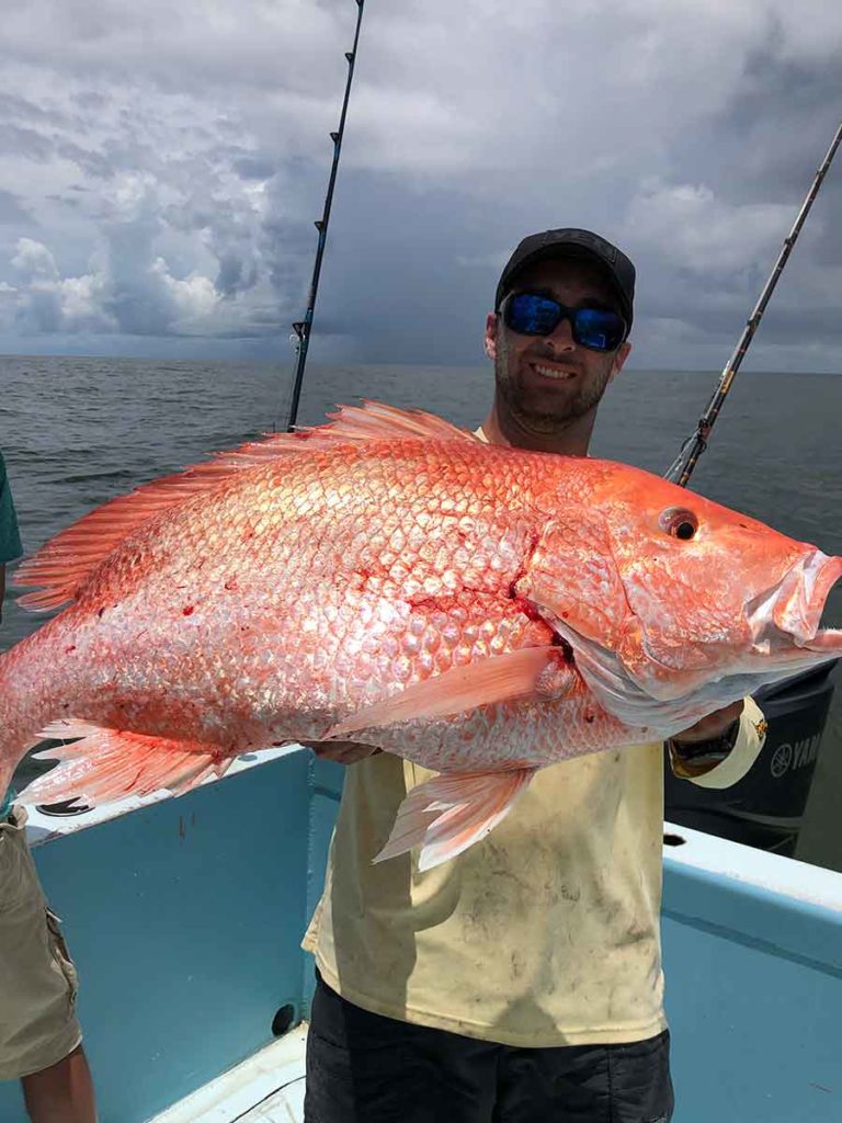man holding red snapper fish that he caught in the gulf of mexico on the offshore fishing charter boat of paradise outfitters in venice la