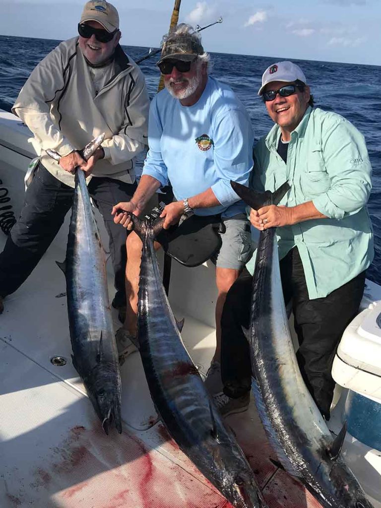 three males holding wahoo fish on the charter boat of Paradise Outfitters in Venice, Louisiana