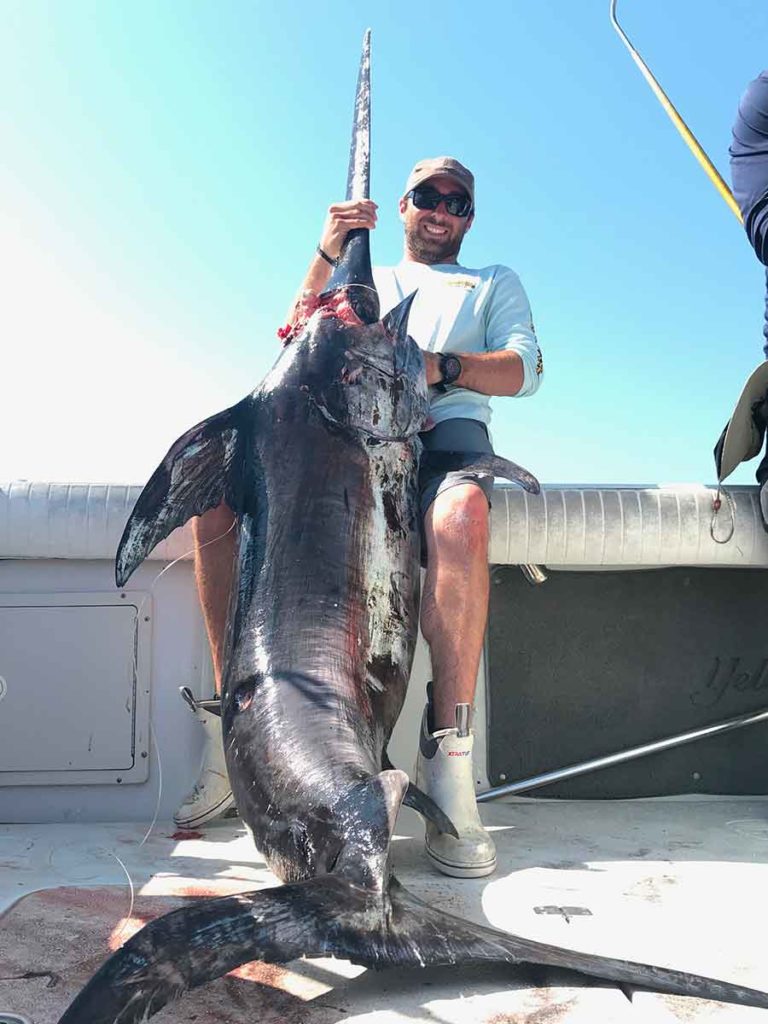 male on a charter boat with big swordfish that he caught in the gulf of mexico during the daytime