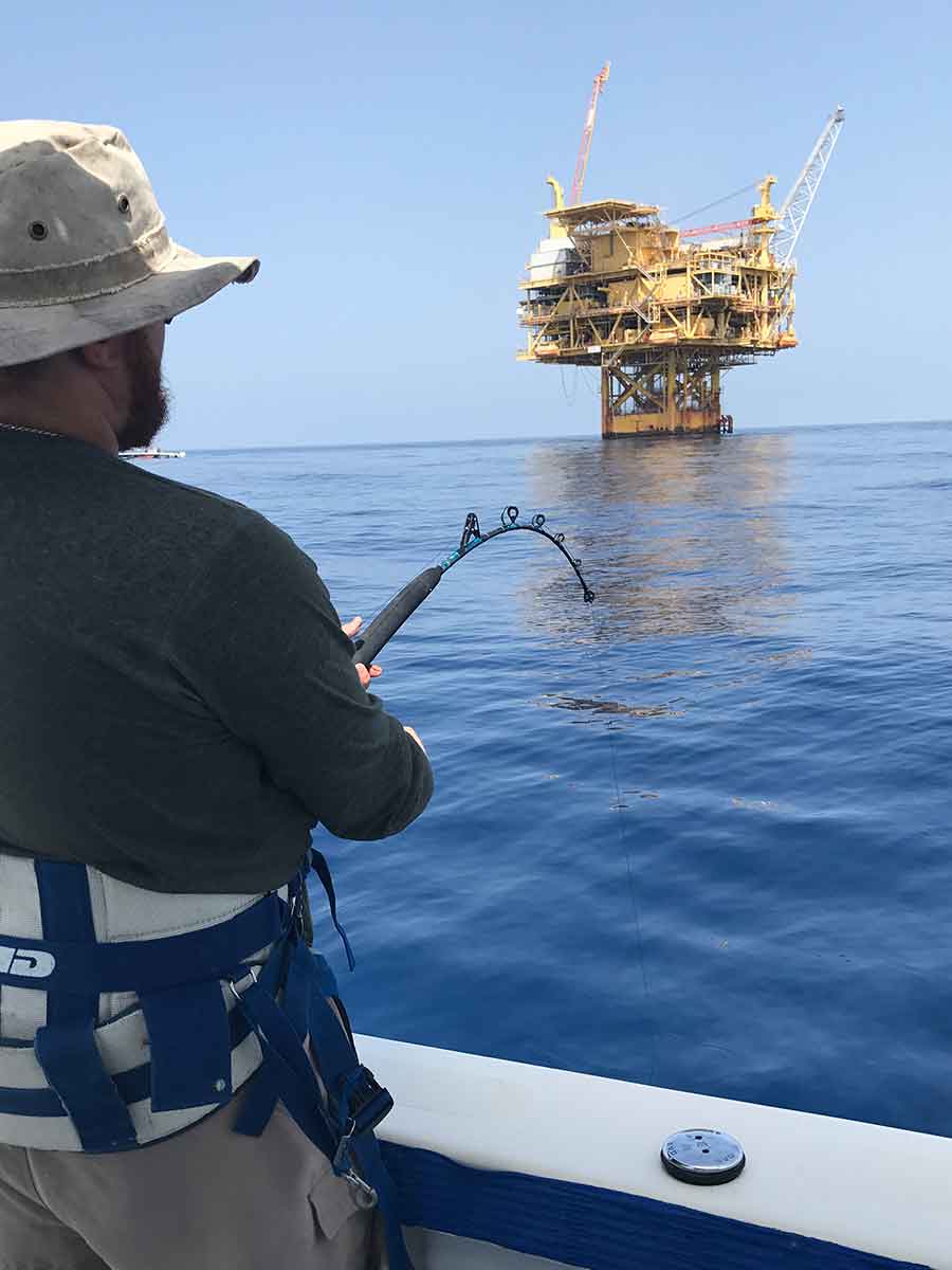 fishing charter customer casting near an oil rig for yellowfin tuna