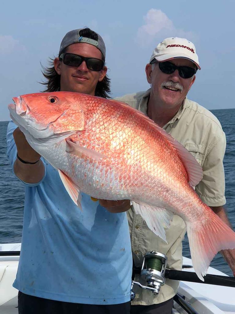 male with paradise outfitters charter boat fishing guide drew bateman holding a red snapper with red and white streaks
