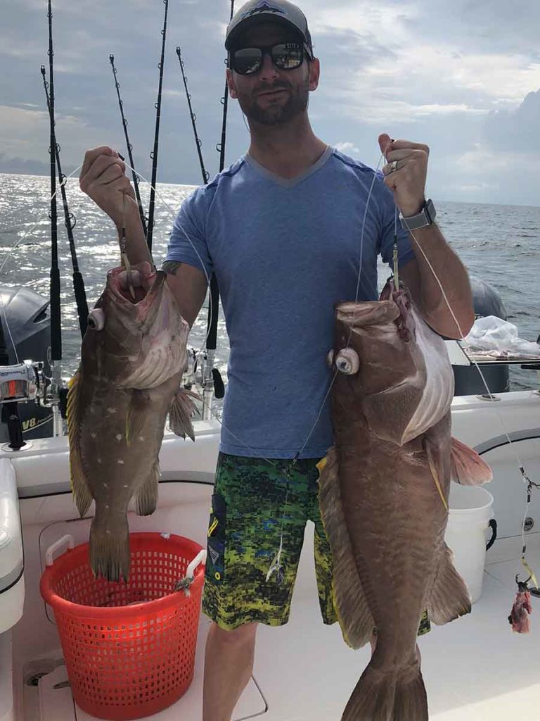 man holdding two huge grouper fish that he caught in the gulf of mexico aboard Paradise Outfitters Charter Fishing boat in Venice, Louisiana